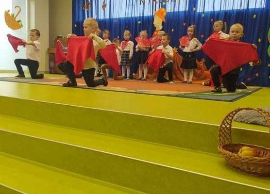 Występ grupy jeżyków. Chłopcy klękają podczas tańca i trzymają czerwone chusty.